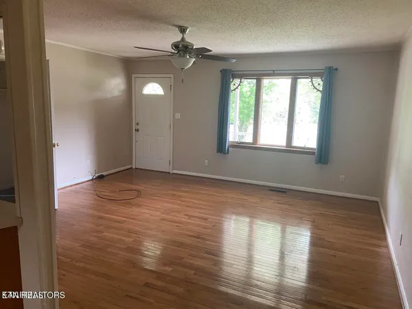 a view of an empty room with wooden floor and a window