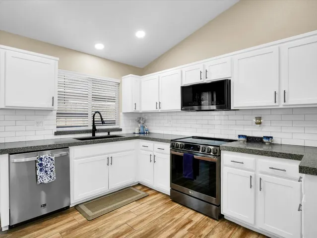 a kitchen with stainless steel appliances granite countertop a stove a sink and white cabinets
