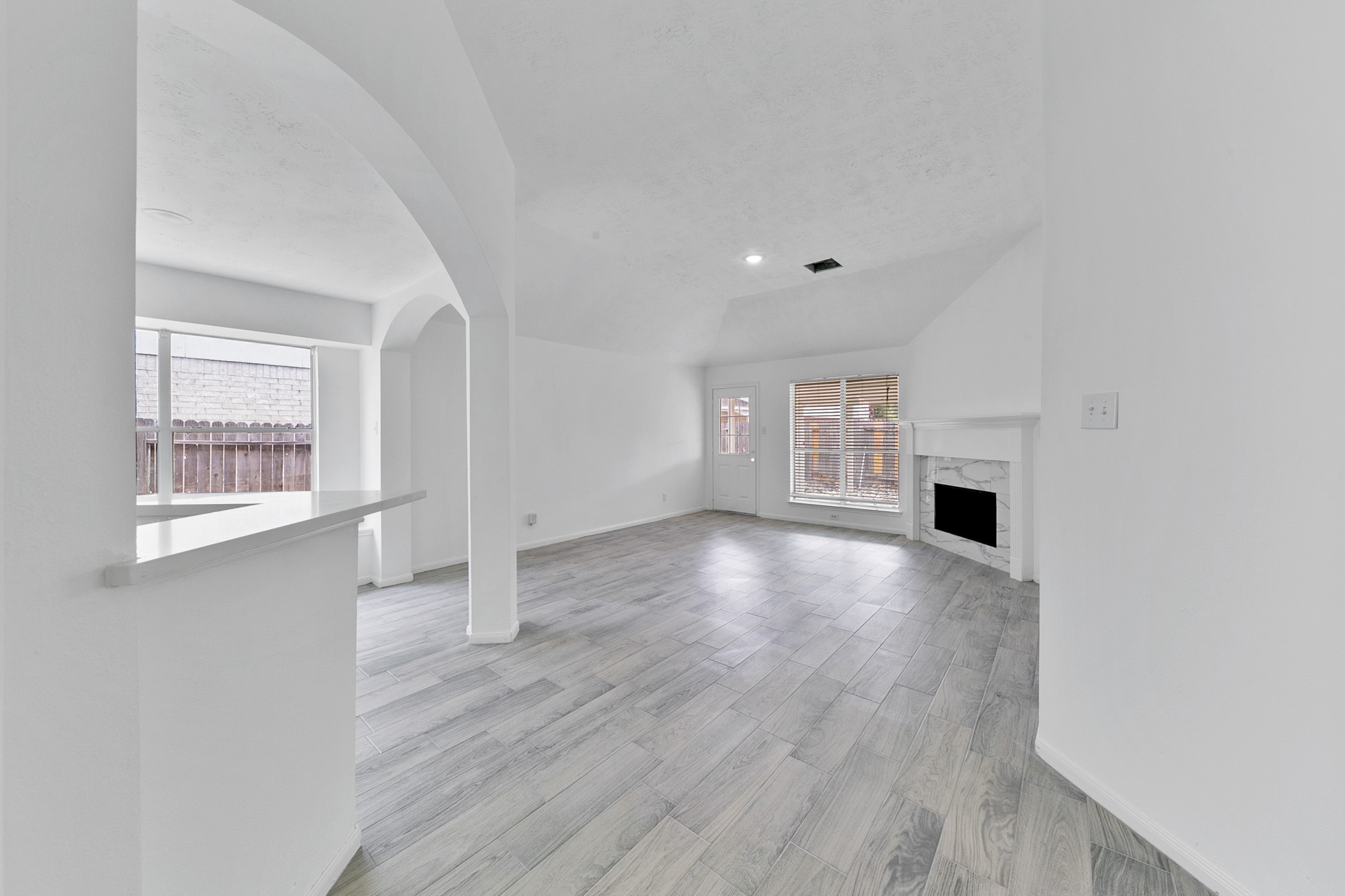 12014 Raven View Drive Houston, TX 77067 - Photo 13 of 29 Bright and spacious living area featuring light wood flooring, a cozy fireplace, and large windows for natural light. The open layout includes an archway leading to a dining area, creating an airy and inviting atmosphere.