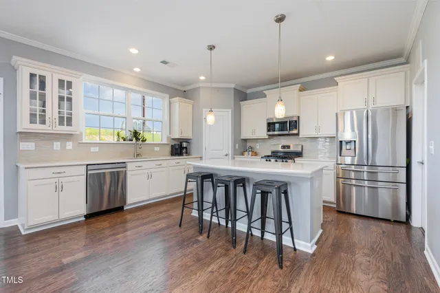 a kitchen with stainless steel appliances granite countertop a refrigerator a sink dishwasher a stove and white cabinets with wooden floor