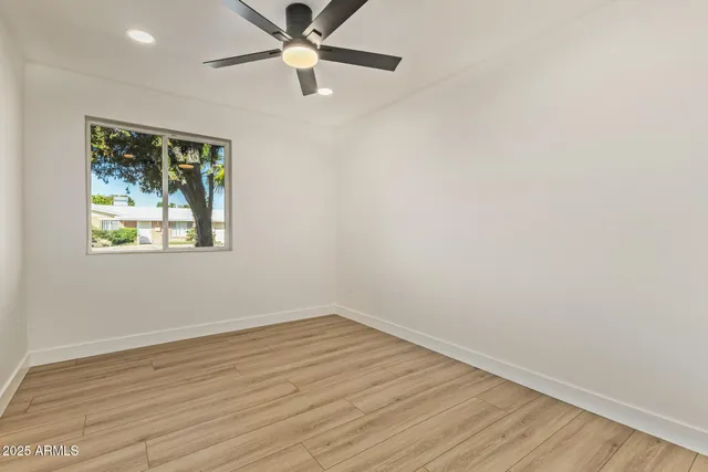an empty room with wooden floor ceiling fan and windows