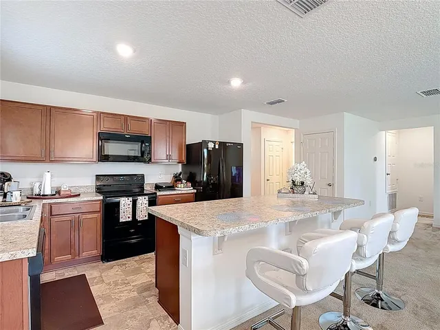 a kitchen with stainless steel appliances granite countertop a stove top oven a sink a refrigerator a dining table and chairs with wooden floor