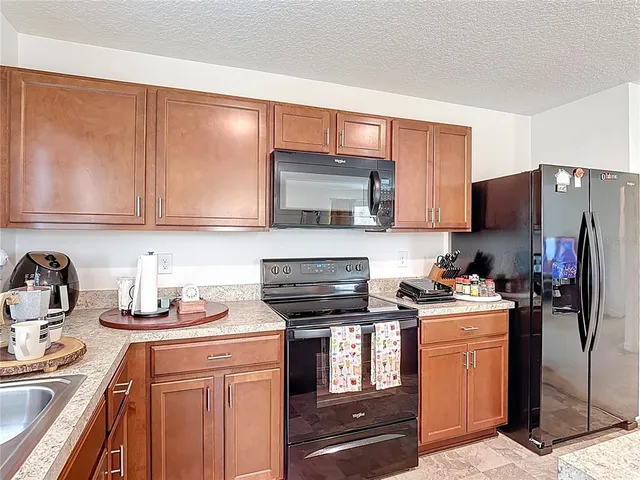 a kitchen with stainless steel appliances granite countertop a stove top oven a sink dishwasher and a refrigerator with wooden cabinets