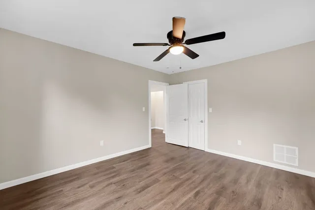 a view of an empty room with wooden floor and a ceiling fan