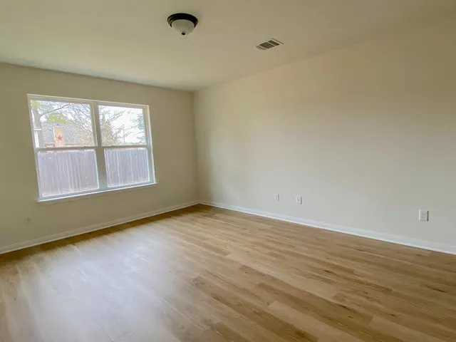 a view of an empty room with wooden floor and a window