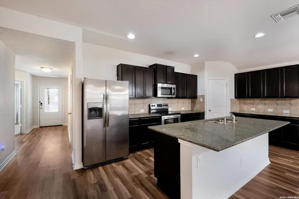 a kitchen with granite countertop a refrigerator a sink a stove a microwave and wooden floor