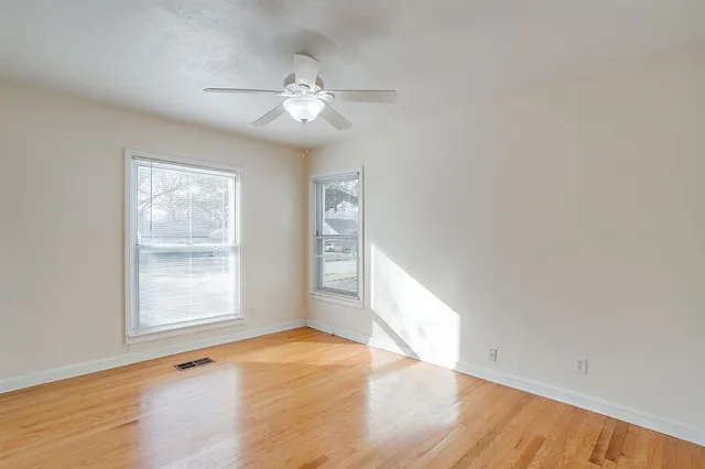 an empty room with wooden floor chandelier fan and windows