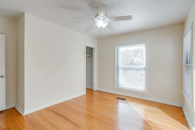 an empty room with wooden floor chandelier fan and windows
