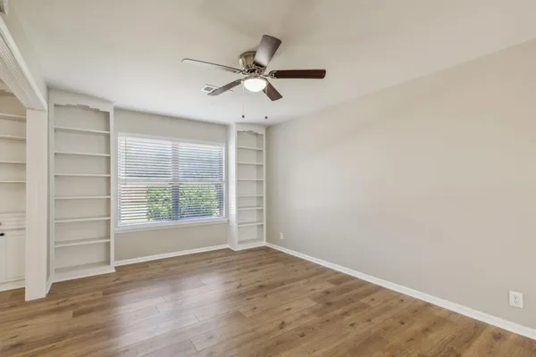 an empty room with wooden floor fan and windows