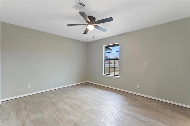 an empty room with wooden floor ceiling fan and windows