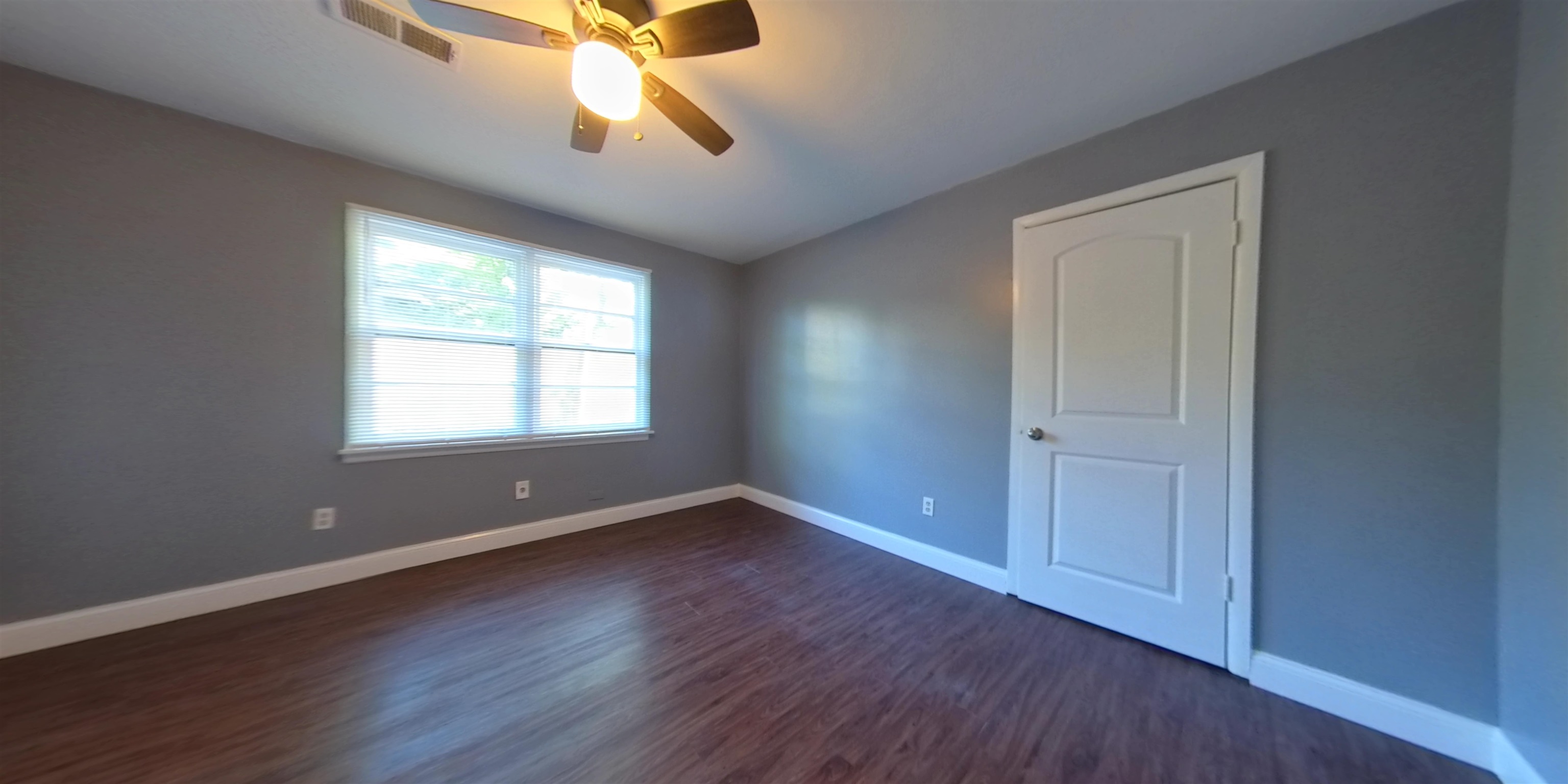 an empty room with wooden floor chandelier fan and windows