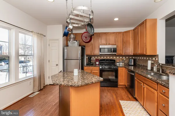 a kitchen with stainless steel appliances granite countertop a refrigerator a stove top oven a sink dishwasher and white cabinets with wooden floor