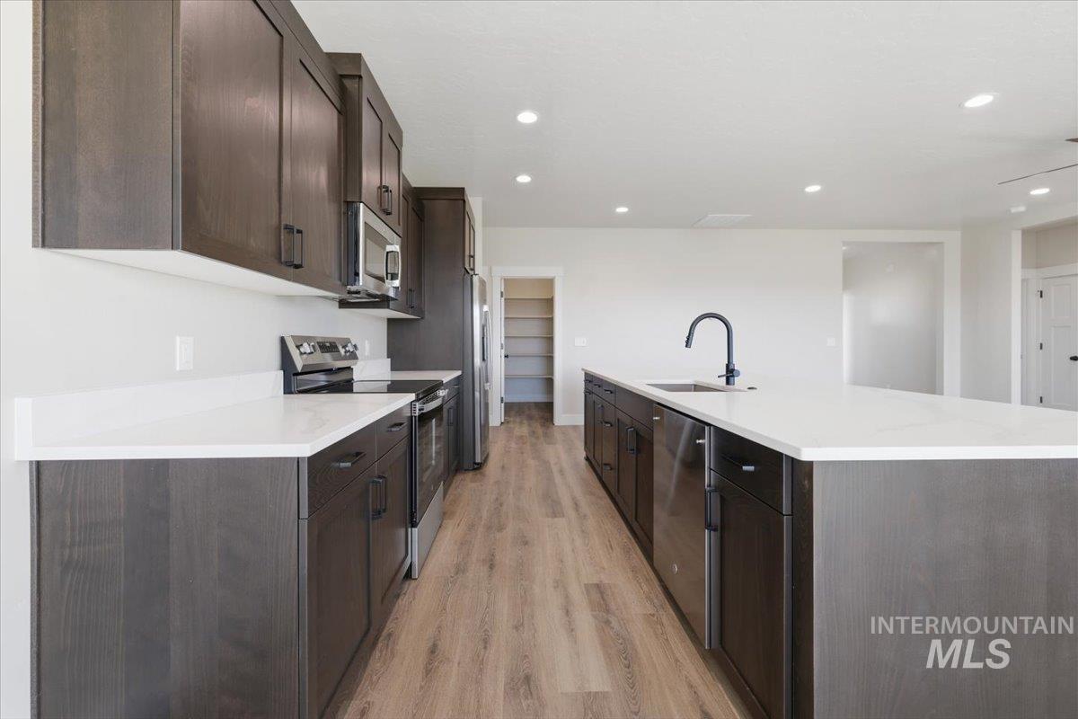 29343 Dixie Road Parma, ID 83660 - Photo 19 of 35 Kitchen featuring stainless steel appliances, an island with sink, dark wood finish cabinets, light wood finished floors, and light stone counters