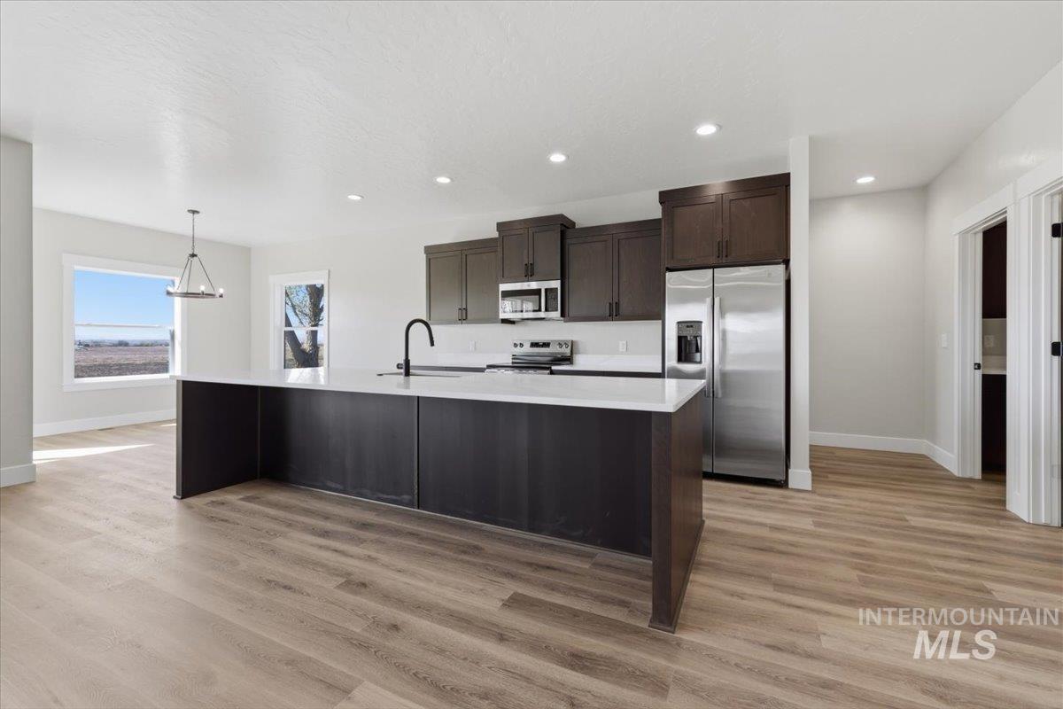 29343 Dixie Road Parma, ID 83660 - Photo 20 of 35 Kitchen with dark wood finish cabinetry, stainless steel appliances, a center island with sink, and light wood-style flooring