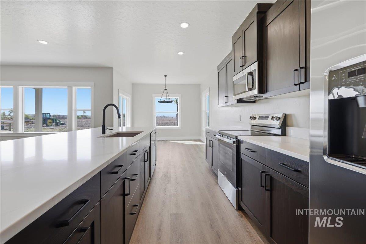29343 Dixie Road Parma, ID 83660 - Photo 21 of 35 Two tone kitchen featuring stainless steel appliances, light wood finished floors, pendant lighting, dual tone cabinets, and light stone countertops