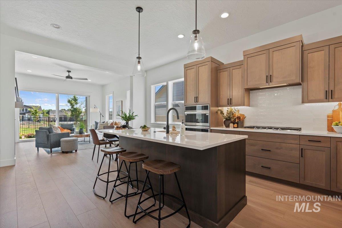 677 North Morning Glory Way Eagle, ID 83616 - Photo 8 of 29 Kitchen featuring hanging light fixtures, a center island with sink, decorative backsplash, light wood-type flooring, and recessed lighting