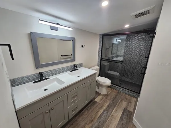 a bathroom with a double vanity sink and mirror with toilet