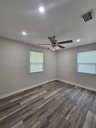 an empty room with wooden floor fan and windows