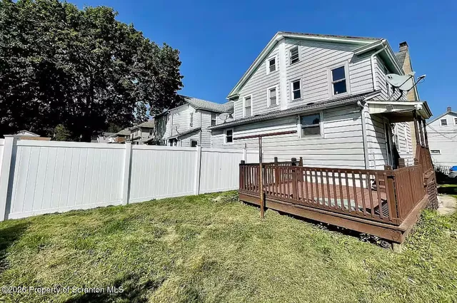 a view of a white house with a small yard and wooden fence
