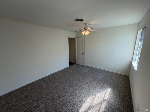 an empty room with a chandelier fan and windows