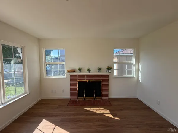 a view of an empty room with wooden floor fireplace and a window