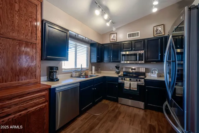 a kitchen with stainless steel appliances granite countertop a refrigerator a sink dishwasher a stove top oven a kitchen island and couches with wooden floor