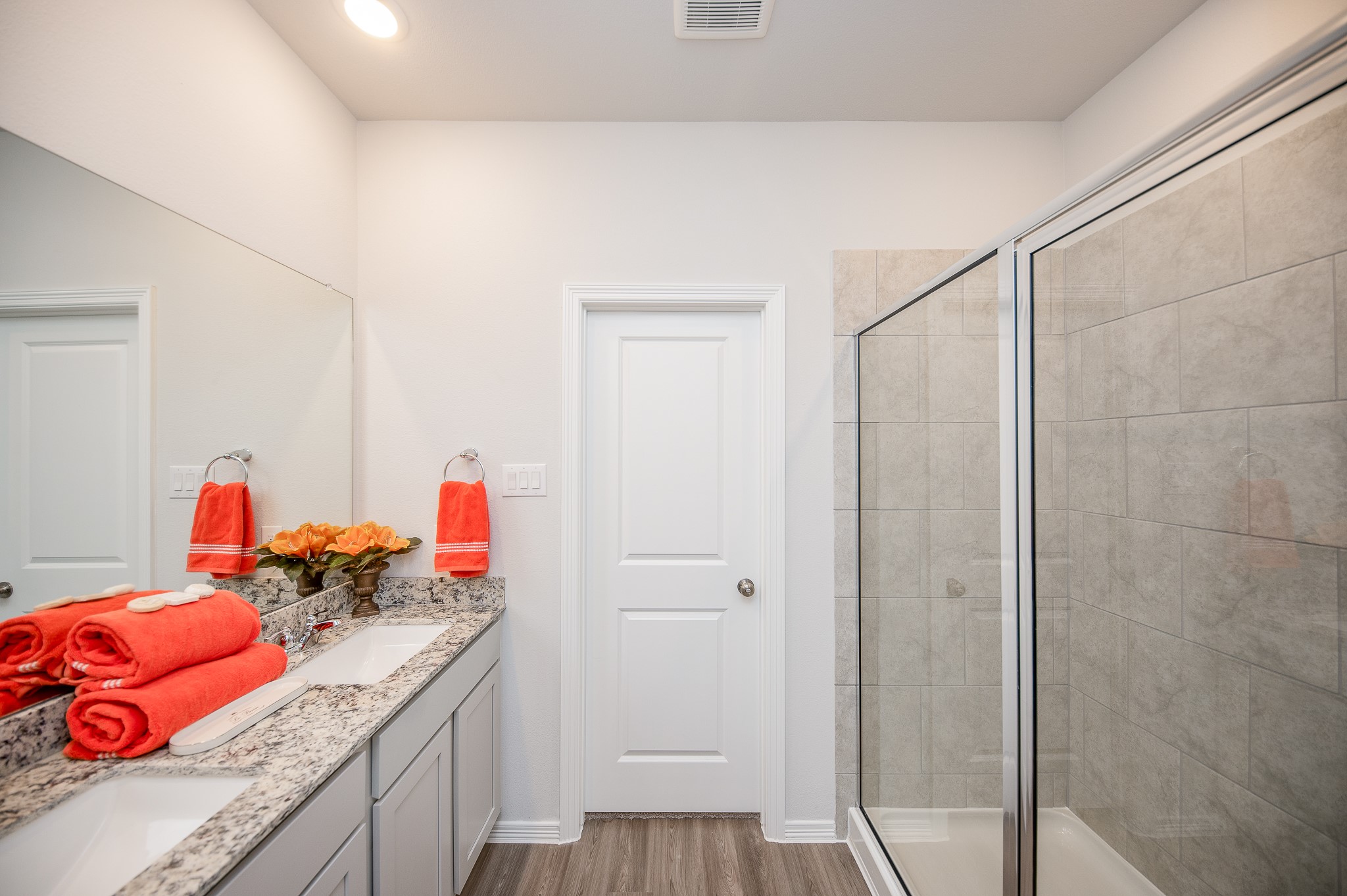 23302 Spring Genesis Lane Katy, TX 77493 - Photo 24 of 32 This bathroom features a double vanity with granite countertops, vibrant orange accents, and a spacious glass-enclosed shower. The design is modern and bright, with ample lighting and neutral tones.