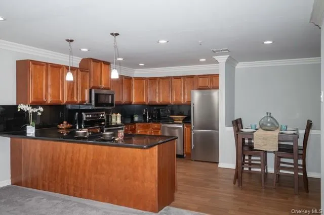 a kitchen with stainless steel appliances granite countertop a refrigerator a sink dishwasher a stove and a dining table with wooden floor