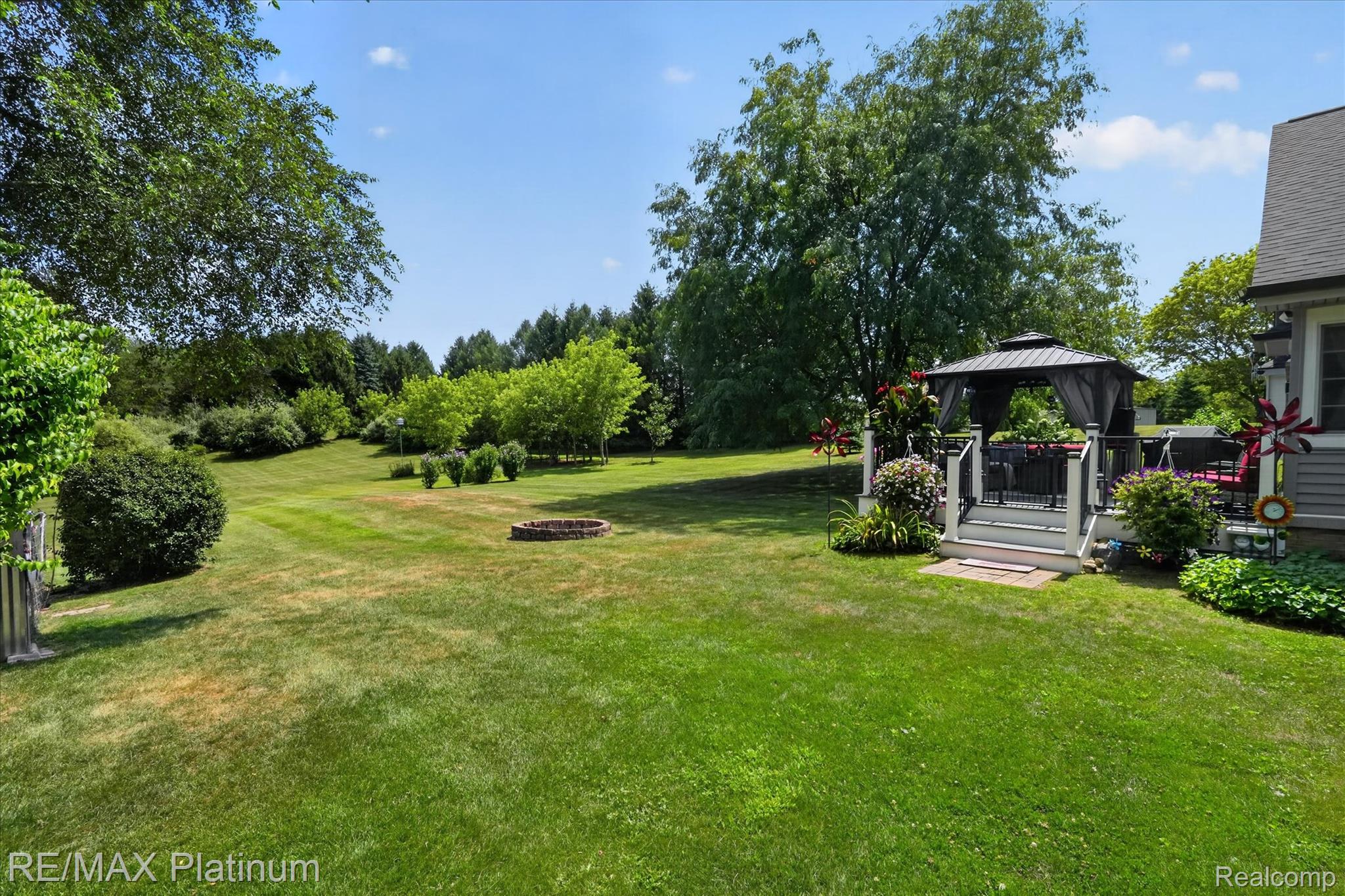 4457 Bradley Road Gregory, MI 48137 - Photo 39 of 79 Expansive green lawn featuring a fire pit area, mature trees, and landscaping