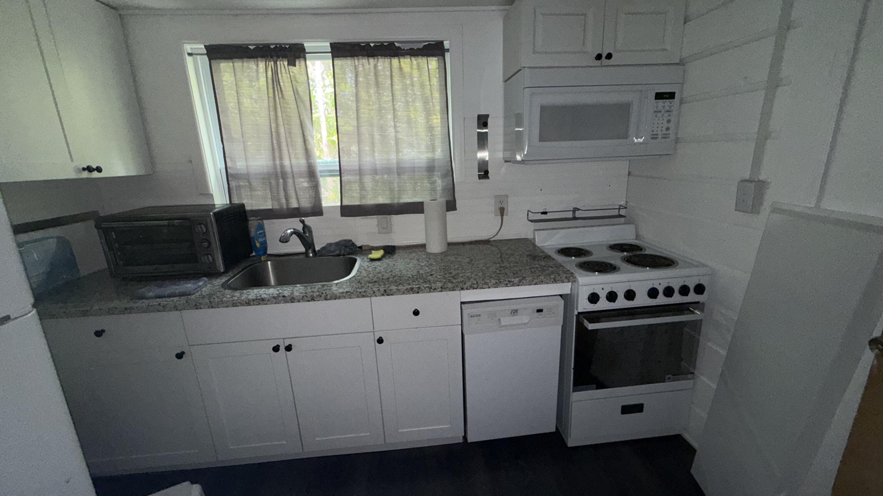 91790 Overseas Highway, Unit BACK Tavernier, FL 33070 - Photo 9 of 13 a kitchen with granite countertop a stove a sink and a microwave