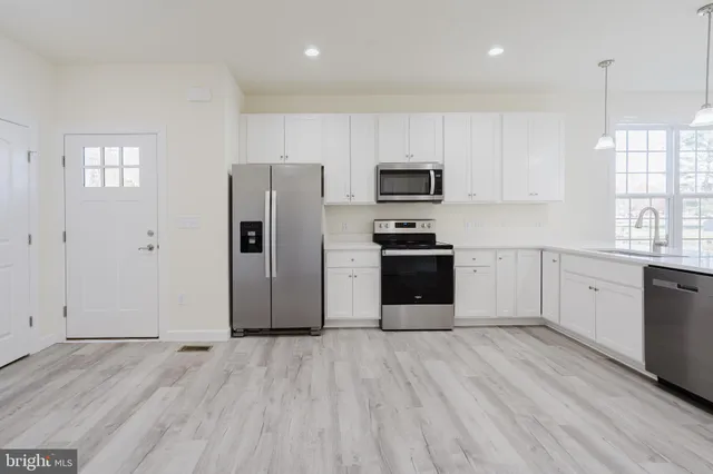 a kitchen with stainless steel appliances granite countertop a refrigerator stove a sink and white cabinets with wooden floor