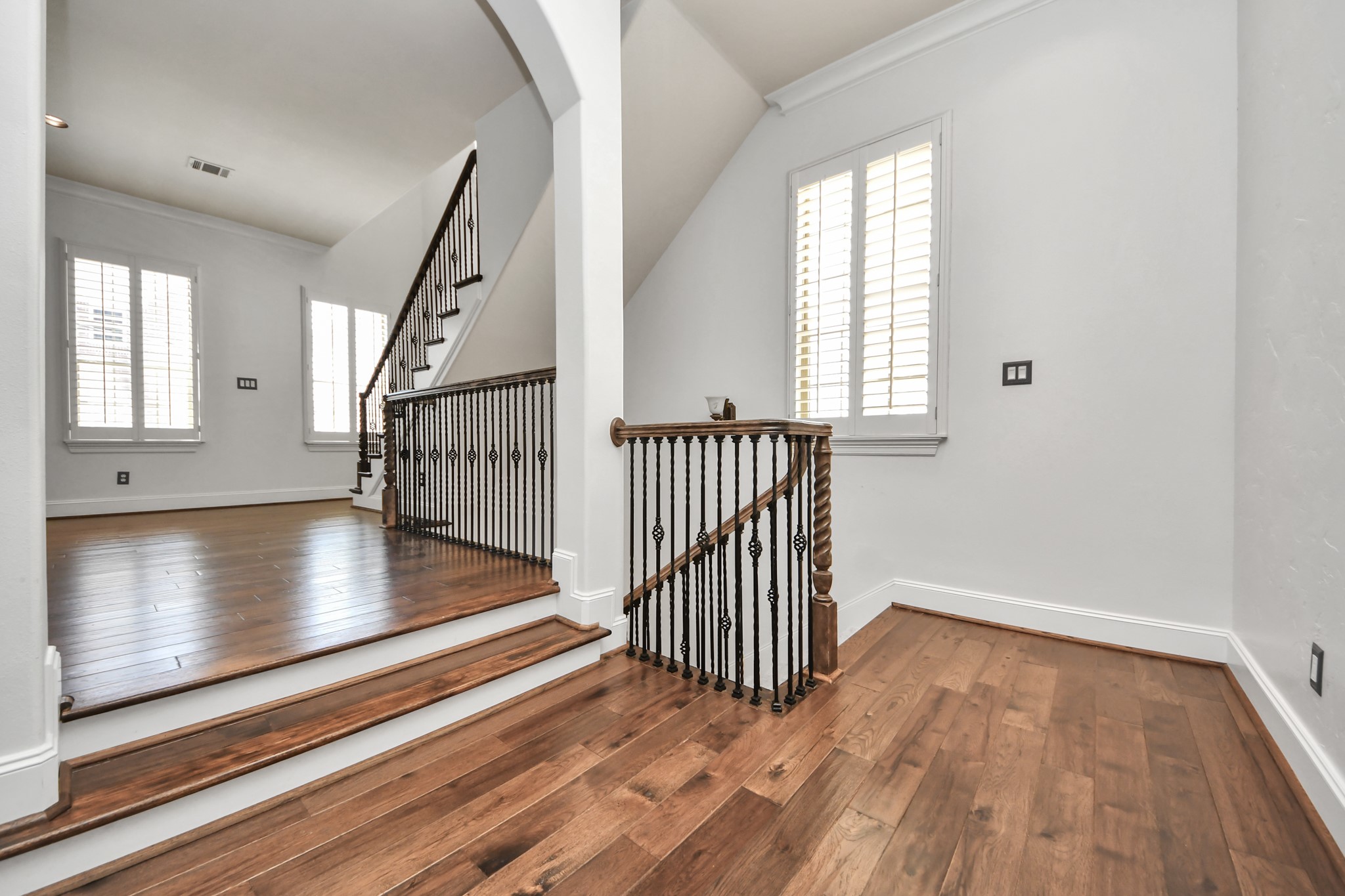 710 Jackson Hill Street Houston, TX 77007 - Photo 9 of 31 This photo showcases a bright, open stairway with wooden floors and decorative iron railings. Large windows with plantation shutters allow natural light to illuminate the space, creating an inviting atmosphere.