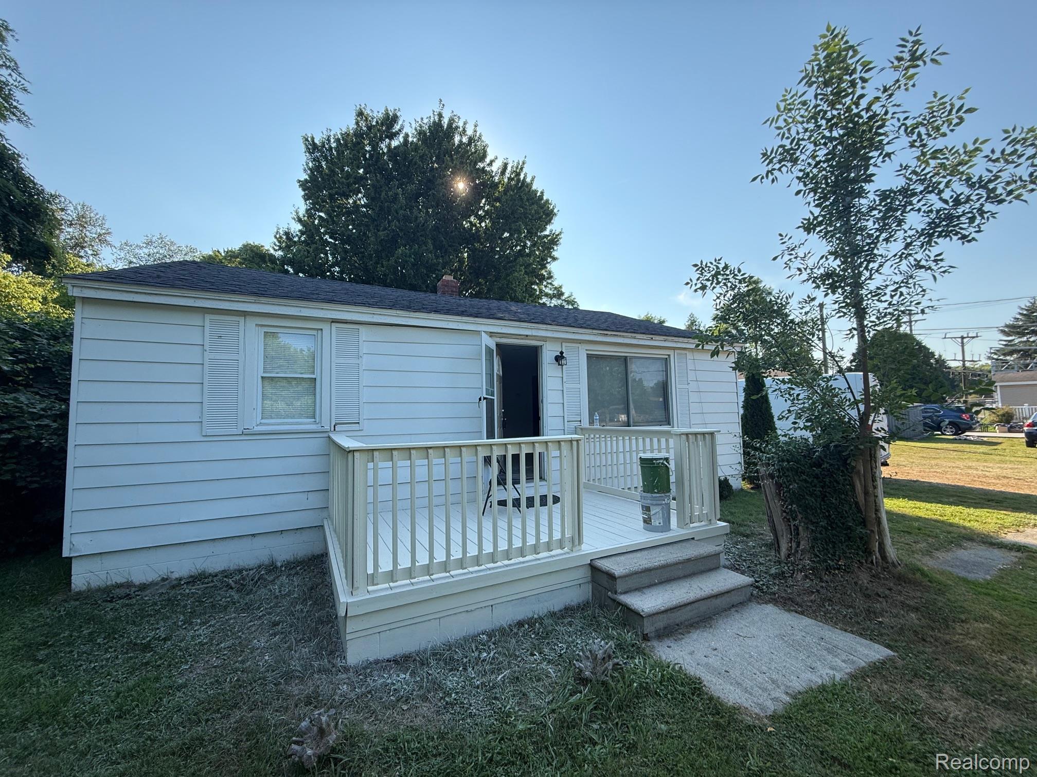 View of front of property featuring a wooden deck, a front lawn, and a shingled roof