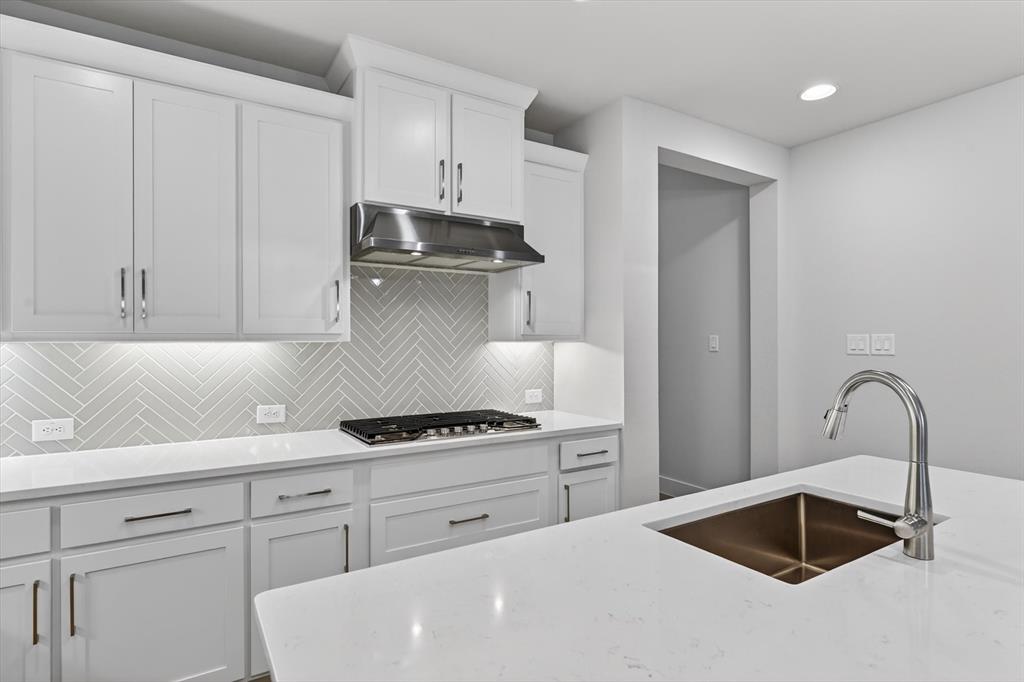4123 Windy Point Court Oak Point, TX 75068 - Photo 17 of 29 Kitchen featuring white shaker-style cabinetry, a herringbone tile backsplash, stainless steel gas cooktop and range hood, and light-toned countertops with a built-in sink and faucet