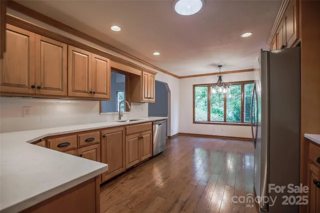 a kitchen with stainless steel appliances granite countertop a refrigerator a sink dishwasher a stove and white countertops with wooden floor