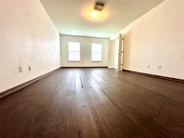 an empty room with wooden floor and windows with curtains