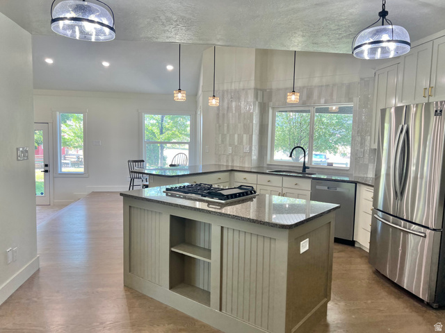 812 East Bates Cyn Road Tooele, UT 84074 - Photo 22 of 144 Open-concept kitchen featuring an island with a built-in gas cooktop, granite countertops, stainless steel appliances, white cabinetry with gold-tone hardware, and a tile backsplash