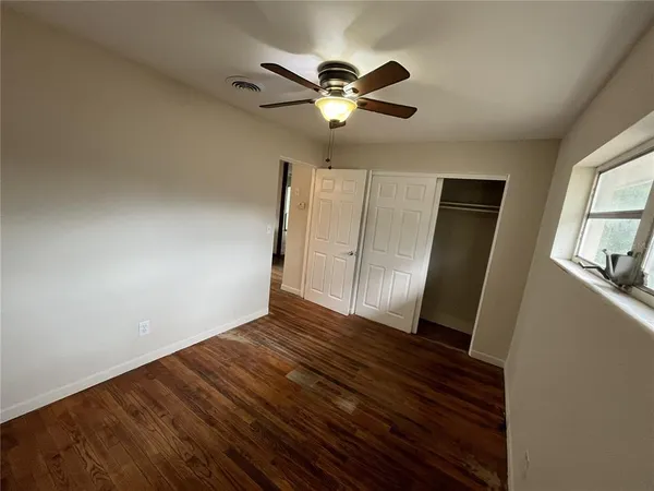 a view of an empty room with wooden floor and a ceiling fan