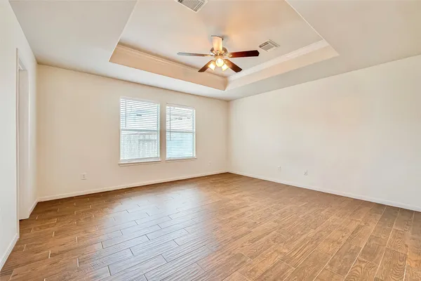 an empty room with wooden floor ceiling fan and windows