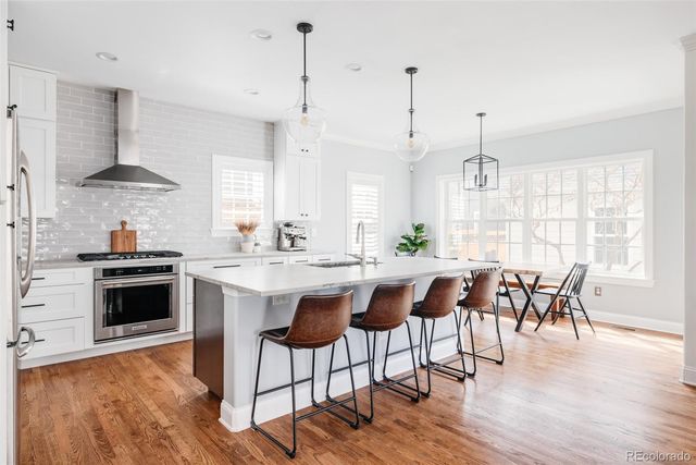 a kitchen with stainless steel appliances granite countertop a stove a refrigerator a kitchen island a dining table and chairs with wooden floor