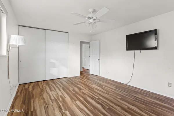 a view of empty room with wooden floor and fan