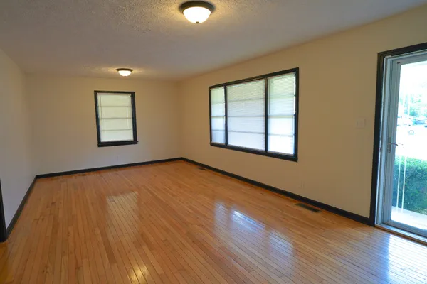 a view of an empty room with wooden floor and a window