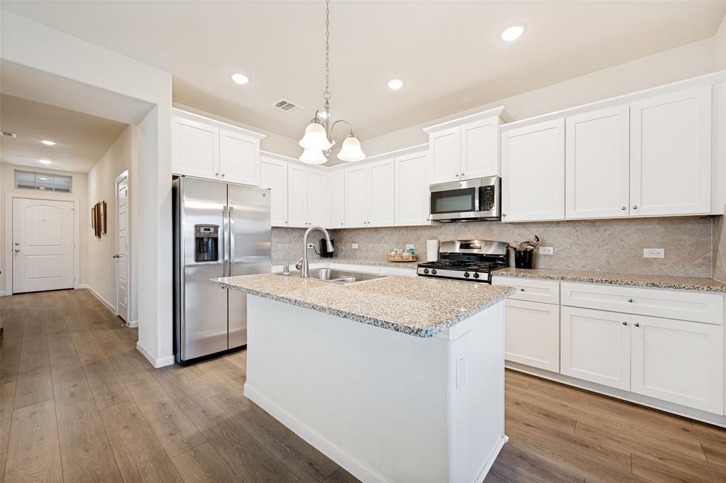413 Wiggins Way Van Alstyne, TX 75495 - Photo 3 of 25 Open-concept kitchen featuring white cabinetry, granite countertops, stainless steel appliances, and wood-finish flooring