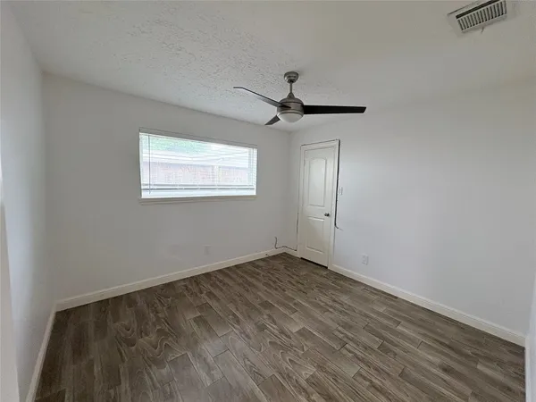 an empty room with wooden floor ceiling fan and windows