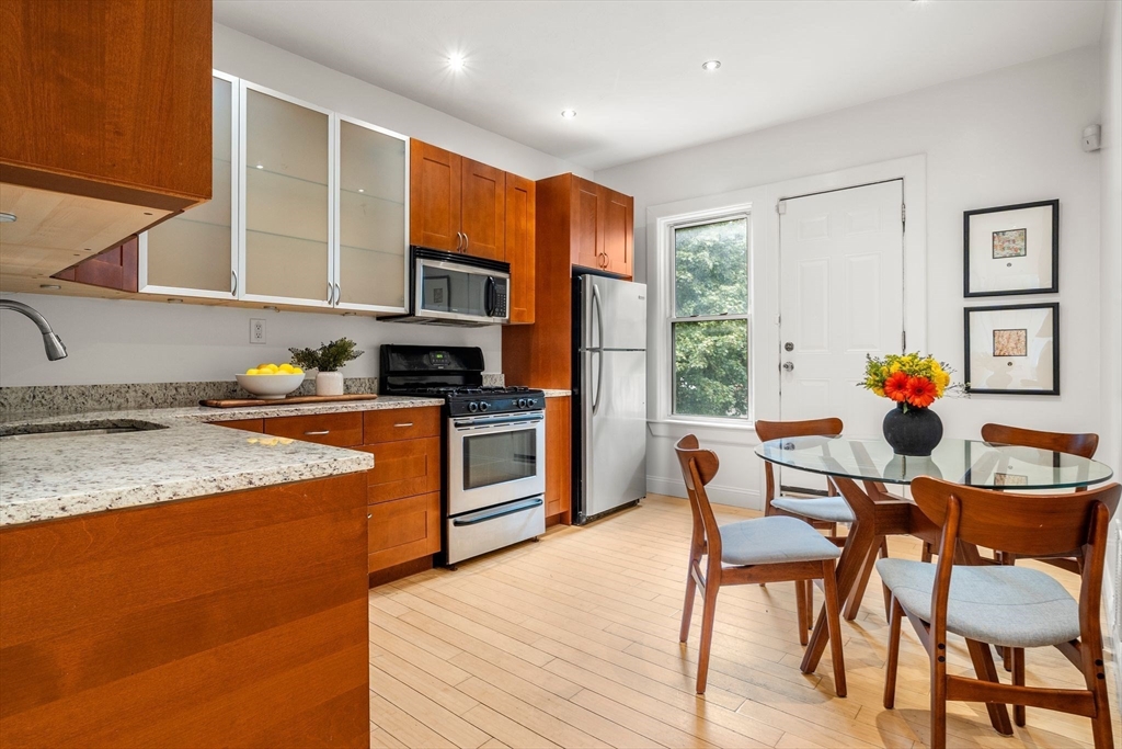 178 Hyde Park Avenue, Unit 3 Boston, MA 02130 - Photo 7 of 23 a kitchen with stainless steel appliances granite countertop a stove top oven a sink a dining table and chairs with wooden floor