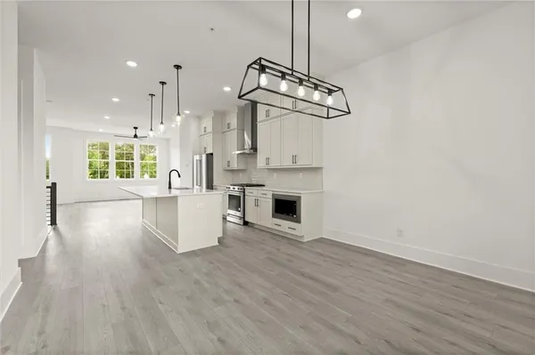 a view of an empty room and kitchen with wooden floor