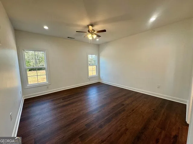 an empty room with wooden floor chandelier fan and windows