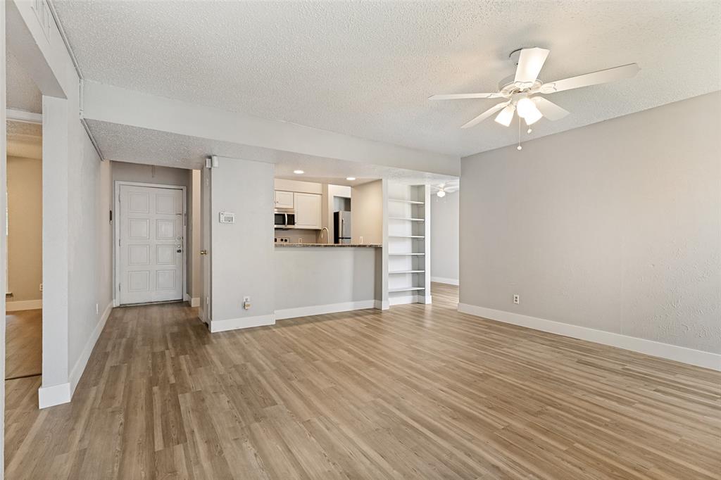 5522 Boca Raton Boulevard, Unit 404 Fort Worth, TX 76112 - Photo 6 of 12 Spacious living area featuring wood-finish flooring, a ceiling fan with integrated lighting, and a built-in shelving unit