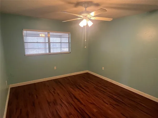 an empty room with wooden floor fan and windows