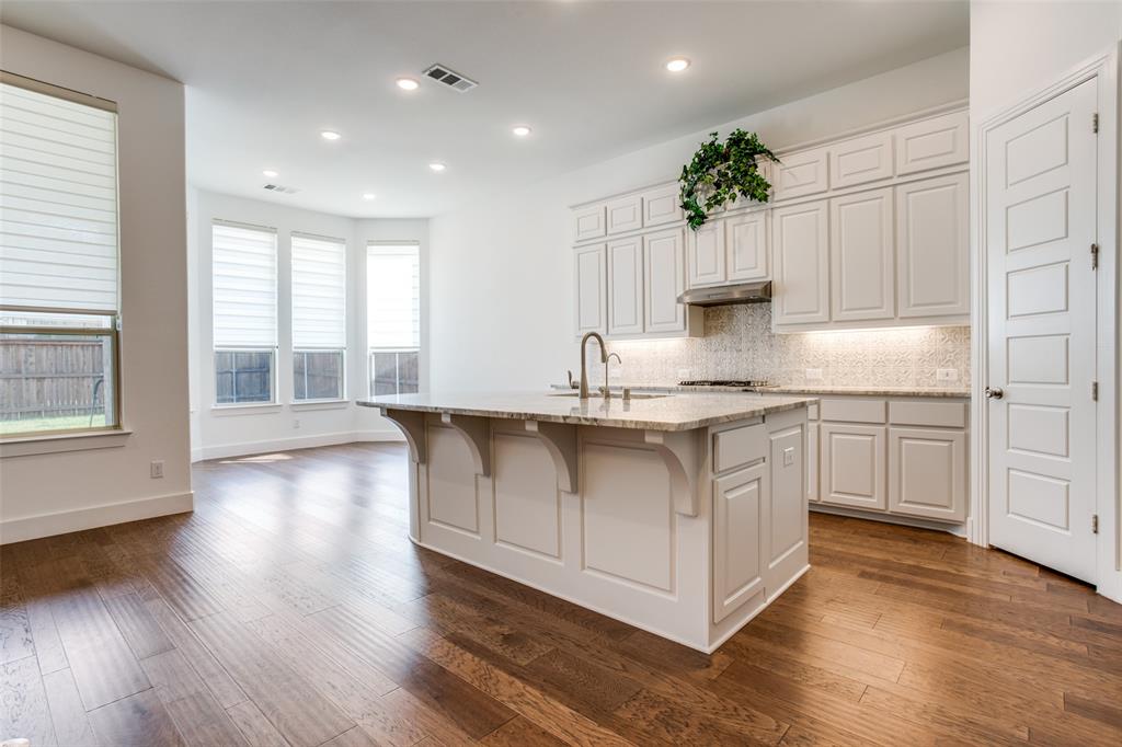 717 Corner Post Path Celina, TX 75009 - Photo 5 of 12 a kitchen with kitchen island granite countertop a stove a sink and white cabinets with wooden floor